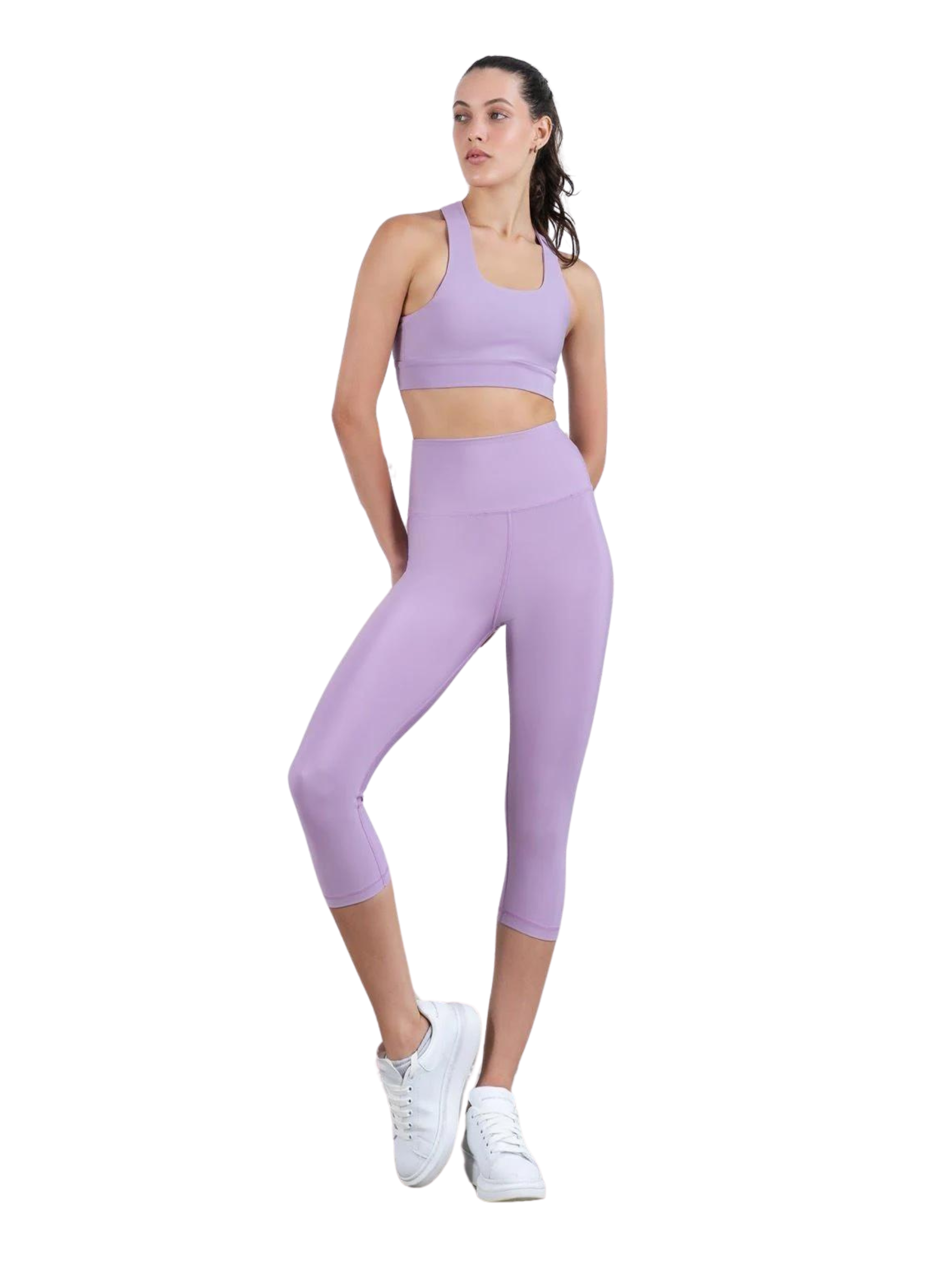 Frau in Capri-Leggings Lismina 4316 mit einem Sport-BH in Lila und weißen Turnschuhen vor weißem Hintergrund.